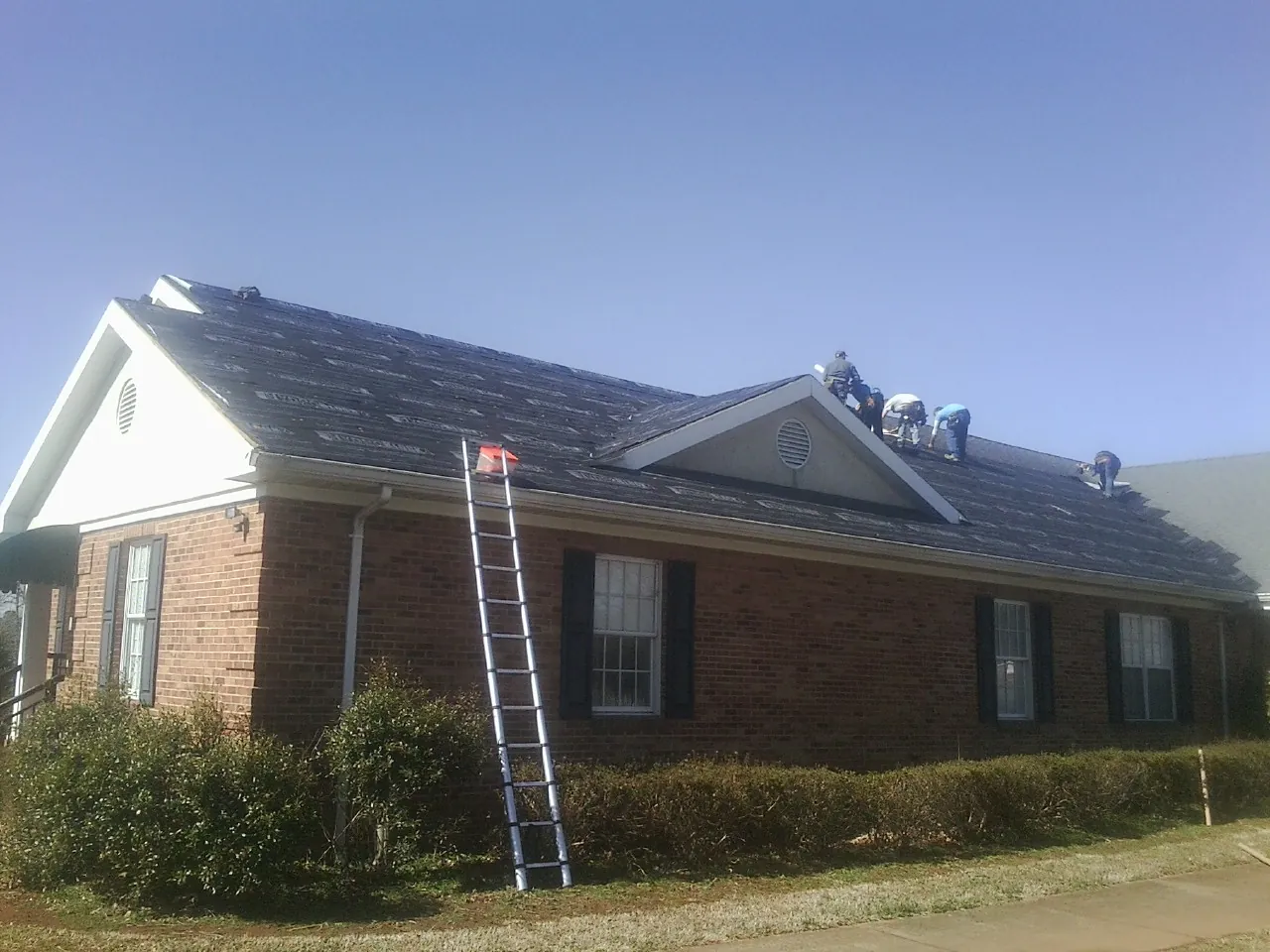 Crew tearing shingles off a brick ranch roof with a ladder set — Metal Roof Repair work by our crew in Bordentown