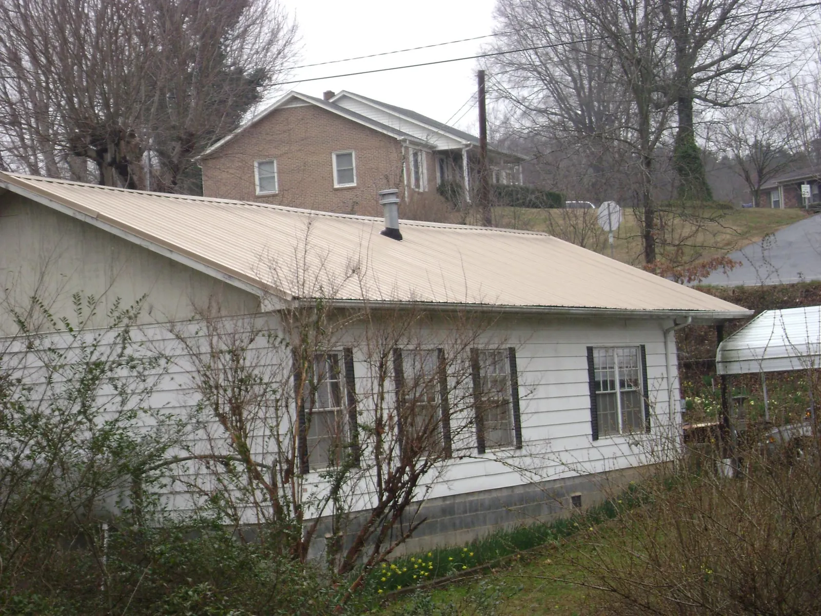 Tan metal roof on a white sided house set into a hillside — Commercial Roofing by Roofing Brothers in Bordentown
